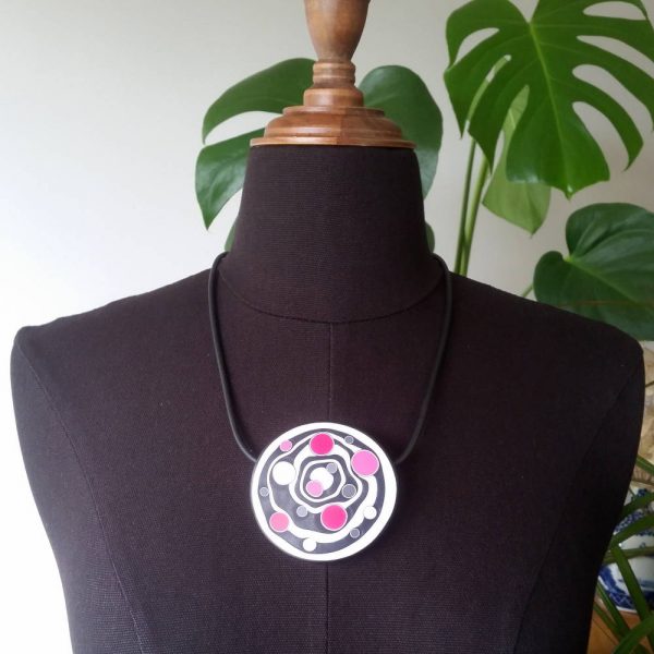 Large handmade pendant with organically-shaped concentric black and white circles, and irregular dots in various pinks. It is approximately 6.6cm in diameter and hangs on a black adjustable cord.