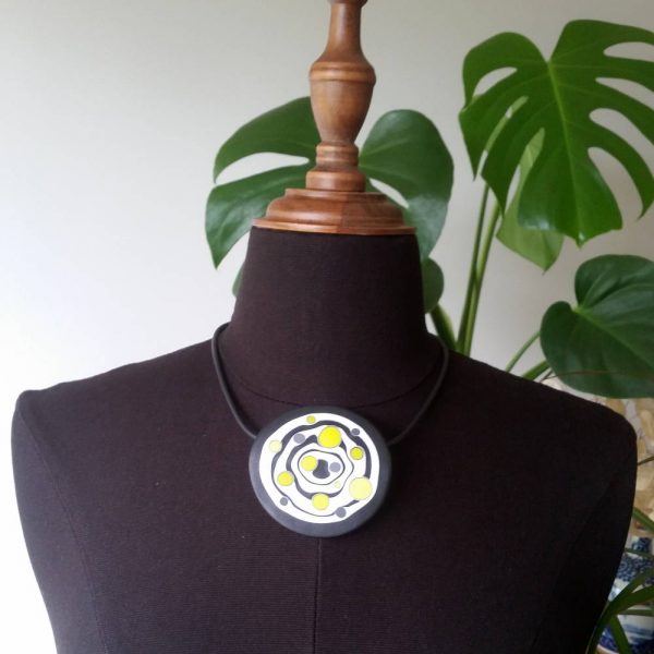 Large handmade pendant with organically-shaped concentric black and white circles, and irregular dots of bright yellow. It is approximately 6.6cm in diameter and hangs on a black adjustable cord.