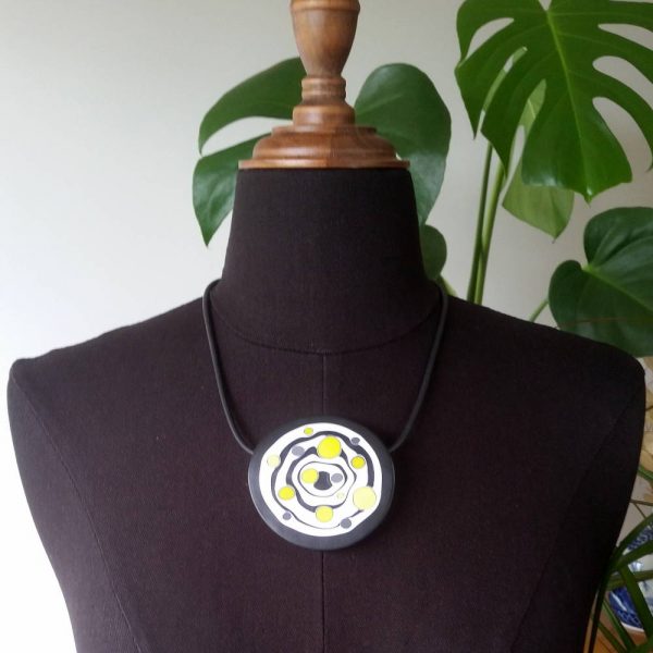 Large handmade pendant with organically-shaped concentric black and white circles, and irregular dots of bright yellow. It is approximately 6.6cm in diameter and hangs on a black adjustable cord.