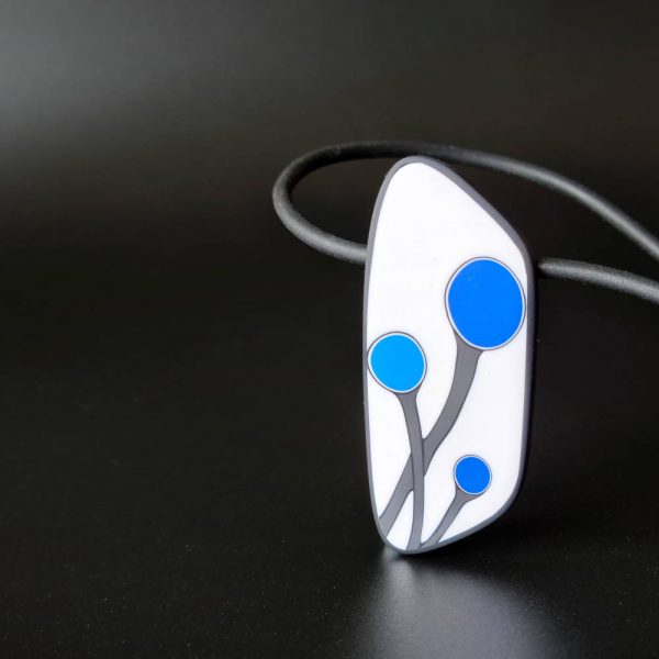 Handmade shield shaped necklace featuring an abstract flower bud motif in blue on a white background, with charcoal border. It is approximately 2.6 cm wide and 6.4cm long and hangs on a black adjustable cord.