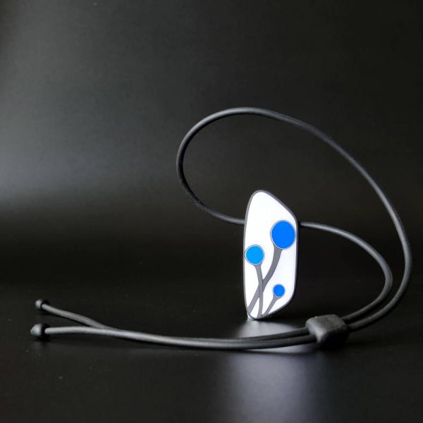 Handmade shield shaped necklace featuring an abstract flower bud motif in blue on a white background, with charcoal border. It is approximately 2.6 cm wide and 6.4cm long and hangs on a black adjustable cord.