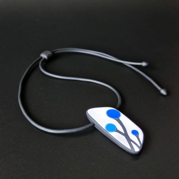 Handmade shield shaped necklace featuring an abstract flower bud motif in blue on a white background, with charcoal border. It is approximately 2.6 cm wide and 6.4cm long and hangs on a black adjustable cord.