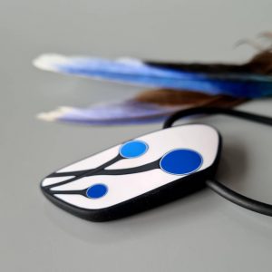 Handmade shield shaped necklace featuring an abstract flower bud motif in blue on a white background, with charcoal border. It is approximately 2.6 cm wide and 6.4cm long and hangs on a black adjustable cord.