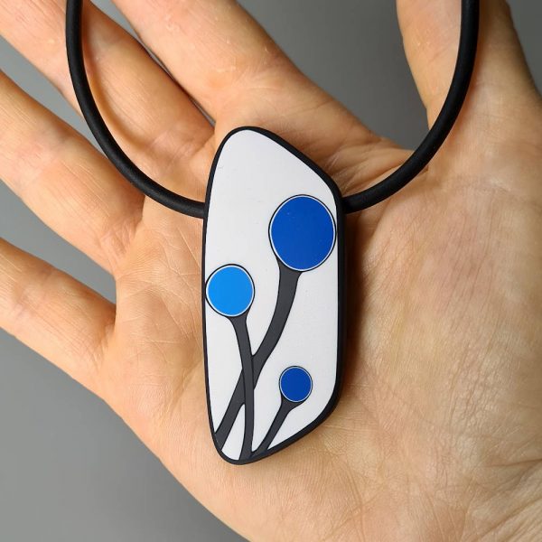Handmade shield shaped necklace featuring an abstract flower bud motif in blue on a white background, with charcoal border. It is approximately 2.6 cm wide and 6.4cm long and hangs on a black adjustable cord.